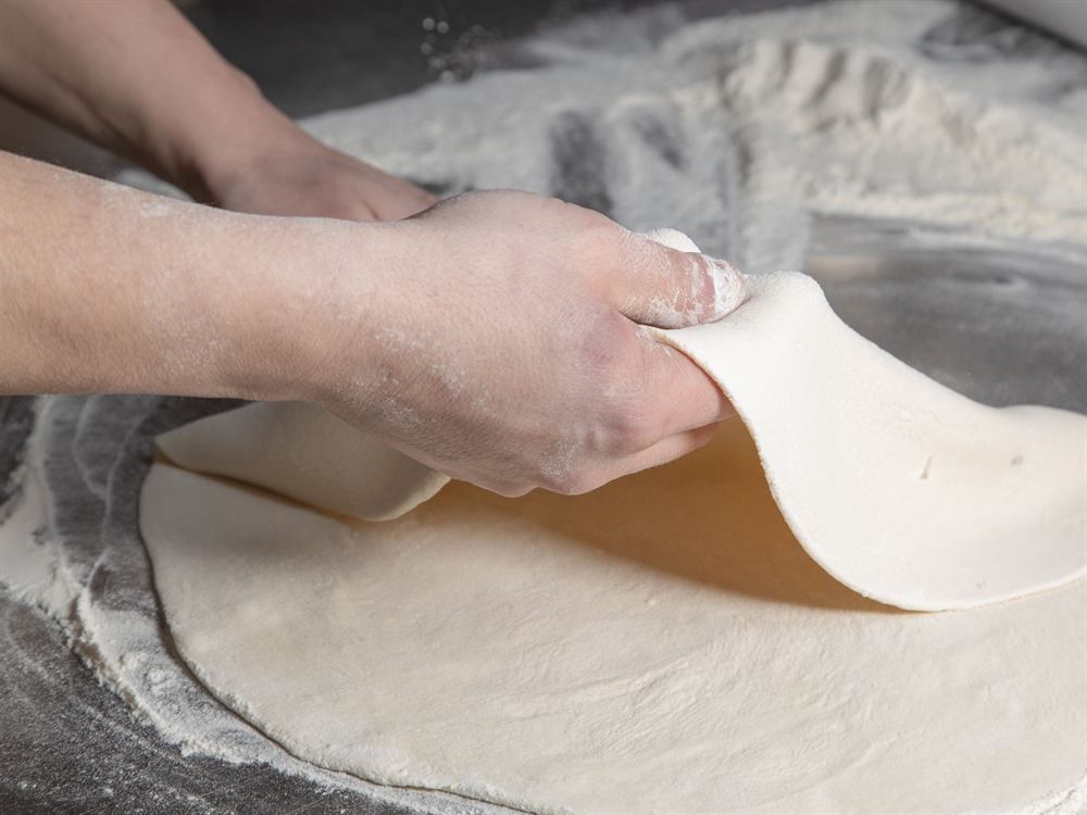 Une pâte à pizza étirée à la main sur un plan de travail fariné, photo d'illustration