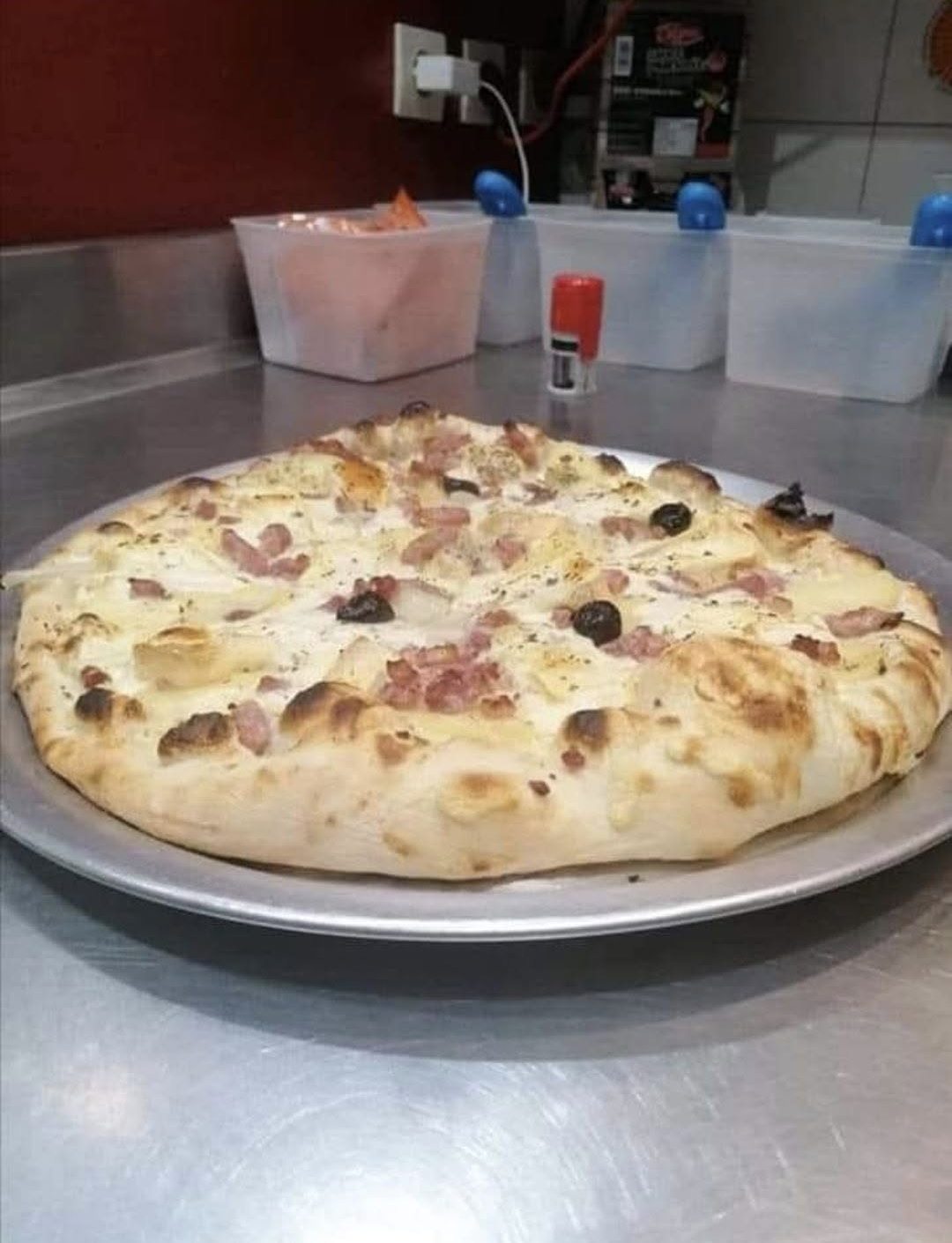 Une pizza crème aux lardons et olives, aux bords bien dorés, posée sur son plateau