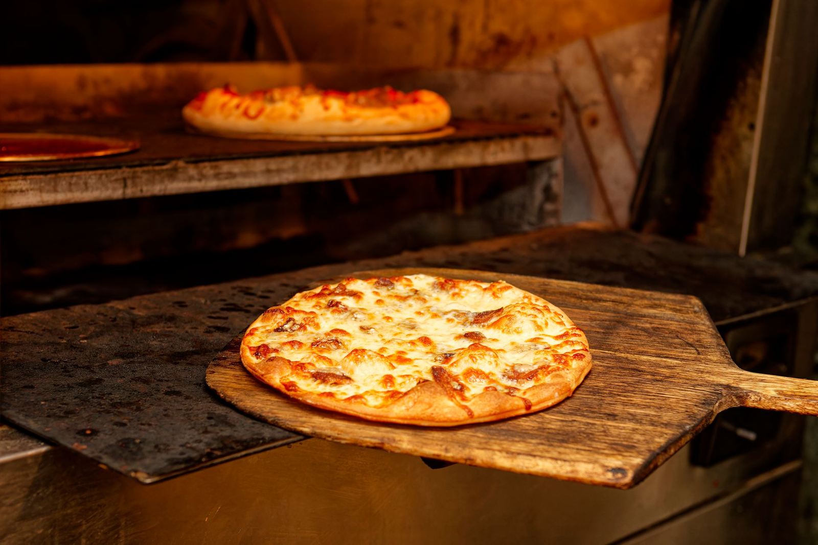 Pizza qui sort du four sur une pelle en bois, photo d'illustration